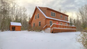 Une cabane en rondins avec une terrasse enneigée et un abri séparé.