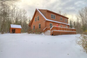 A log cabin with a snow-covered deck and a separate shed.
