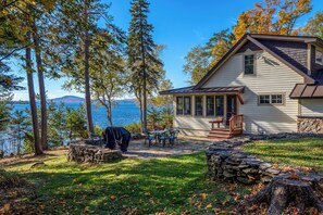 Une maison dotée d’une terrasse en pierre, d’un espace salon extérieur et offrant une vue sur un lac.