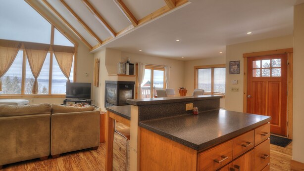 A modern kitchen with a large island, wooden cabinets, and a view of a lake.