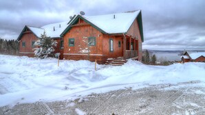 A wooden cabin with a snow-covered roof and a porch, surrounded by snow.