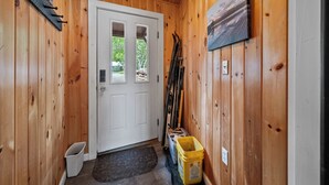 A wooden interior with a white door, a bench, and a yellow trash bin.