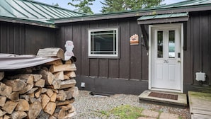 A cabin with a door labeled '26', a window, and a stack of firewood outside.