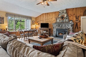 A cozy living room with a stone fireplace, wooden walls, and a television.