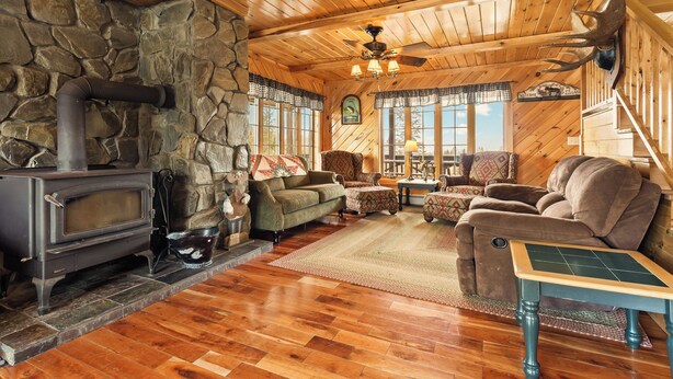A cozy cabin interior with a stone wall, wooden ceiling, a fireplace, and comfortable seating. - Hart | Beautiful family getaway located just three miles from downtown Rangeley (Rangeley)