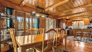 A wooden interior with a dining table and chairs, a kitchen area, and large windows. - Hart | Beautiful family getaway located just three miles from downtown Rangeley (Rangeley)