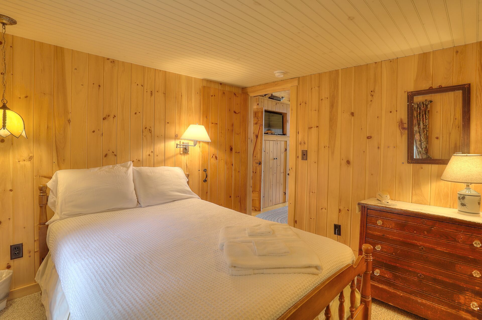 Een slaapkamer met houten lambrisering, een bed, bedlampen, een dressoir en een spiegel.