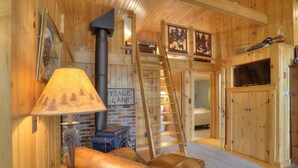 A cozy cabin interior with a fireplace, a wooden staircase, a sofa, and a TV. - Gerstley - Quiet, secluded adorable camp on Loon Lake (Rangeley)