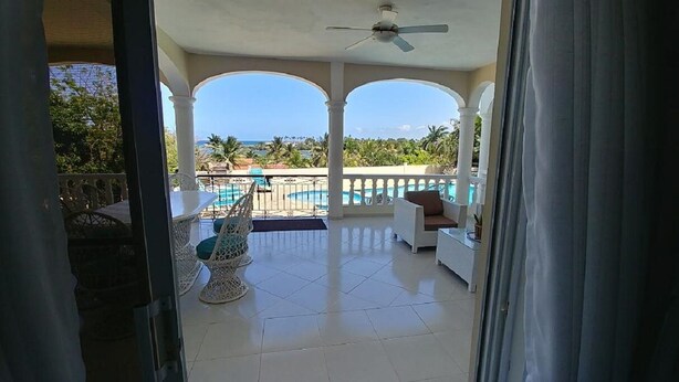 Un balcón con piscina, mobiliario blanco y vista al océano.
