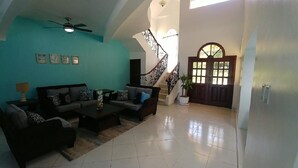 Un salón amplio con un conjunto de sofás, una mesa de centro y una escalera que conduce a un segundo piso.