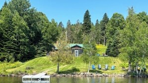 Una baita sul lago con un pontile, circondata da una fitta foresta e un pendio erboso.