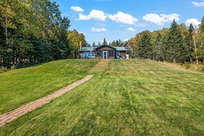 A log cabin with a front porch, a covered deck, and a paved driveway leading to the entrance.
