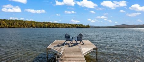 Un muelle de madera que se adentra en un lago, con dos sillas Adirondack mirando al agua.