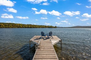 A wooden dock extending into a lake with two Adirondack chairs facing the water.