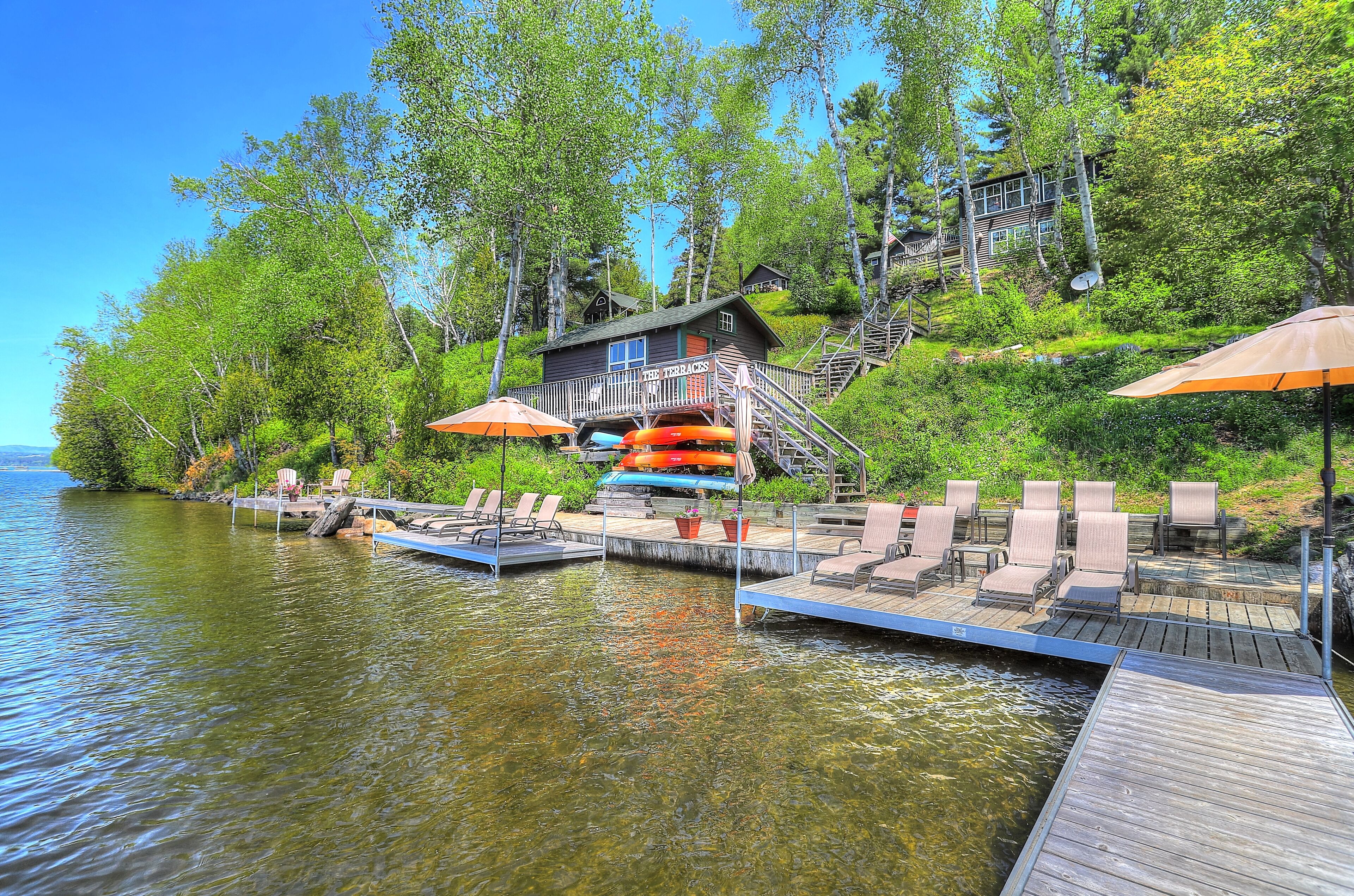 A lakeside cabin with a dock, chairs, and umbrellas.