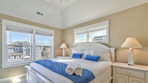 Ein Schlafzimmer mit einem großen Bett, zwei Nachttischen, einem Beistelltisch und Blick auf Häuser durch die Fenster.