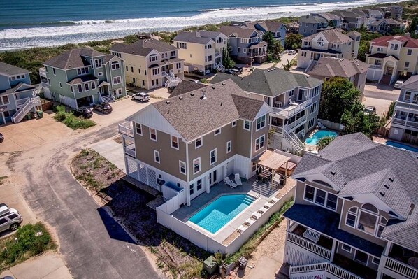 A residential area with houses, a swimming pool, and a beach in the background.
