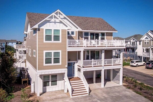 A two-story residential building with a balcony on the upper floor, a front entrance with steps, and a garage.