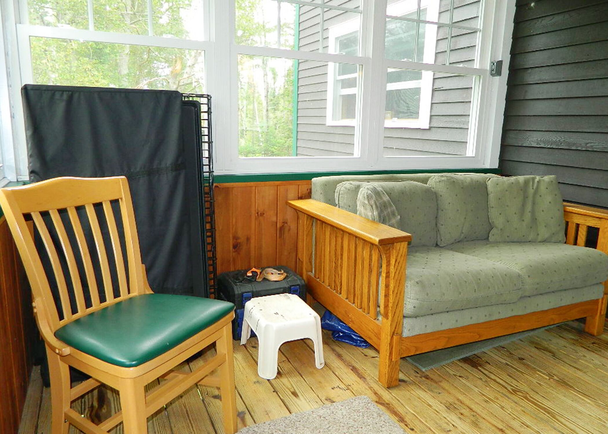 A room with a wooden chair, a small white stool, a green couch, and a window with blinds.