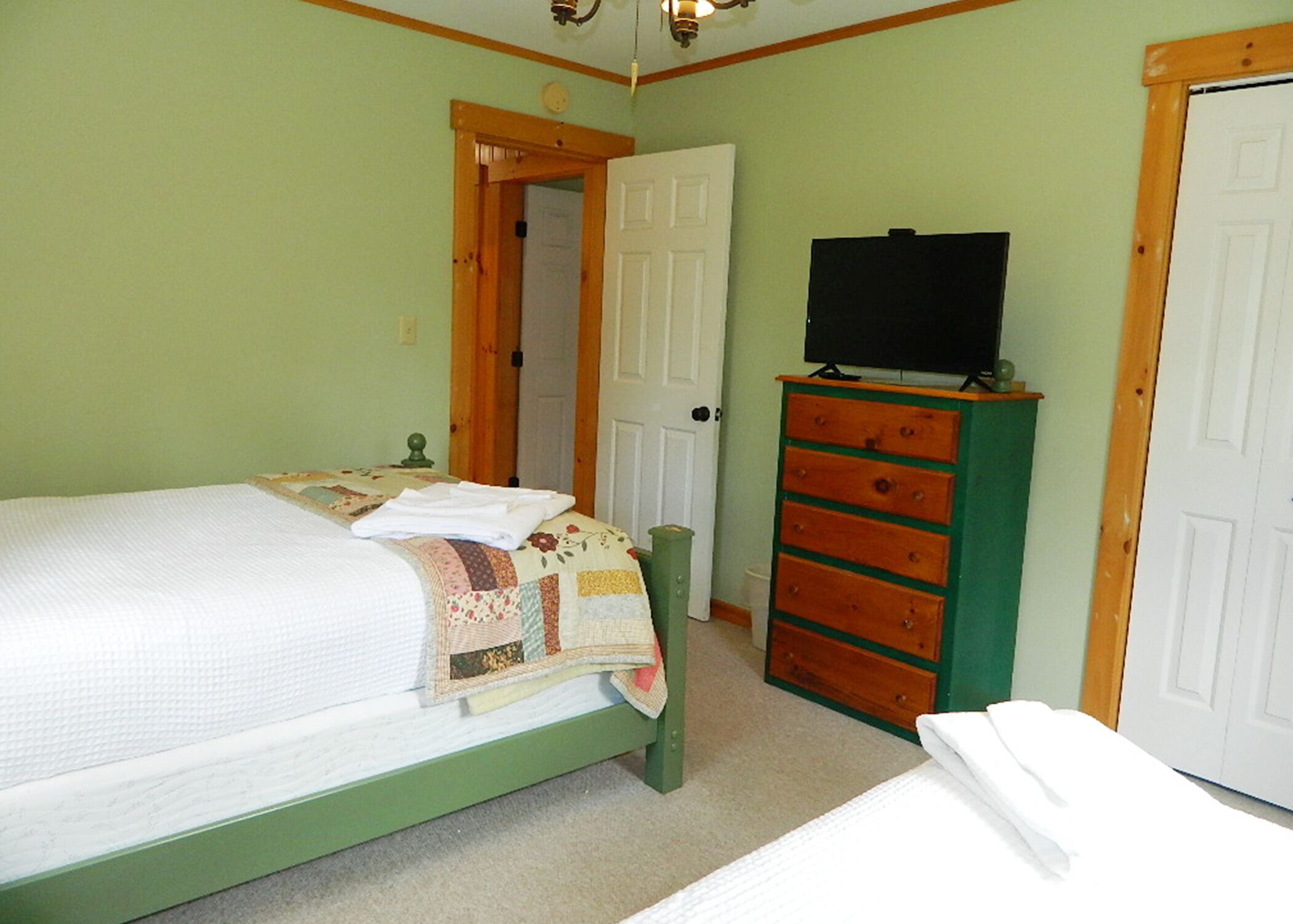 A bedroom with a bed, a dresser, a television, and a door.