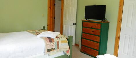 A bedroom with a bed, a dresser, a television, and a door.