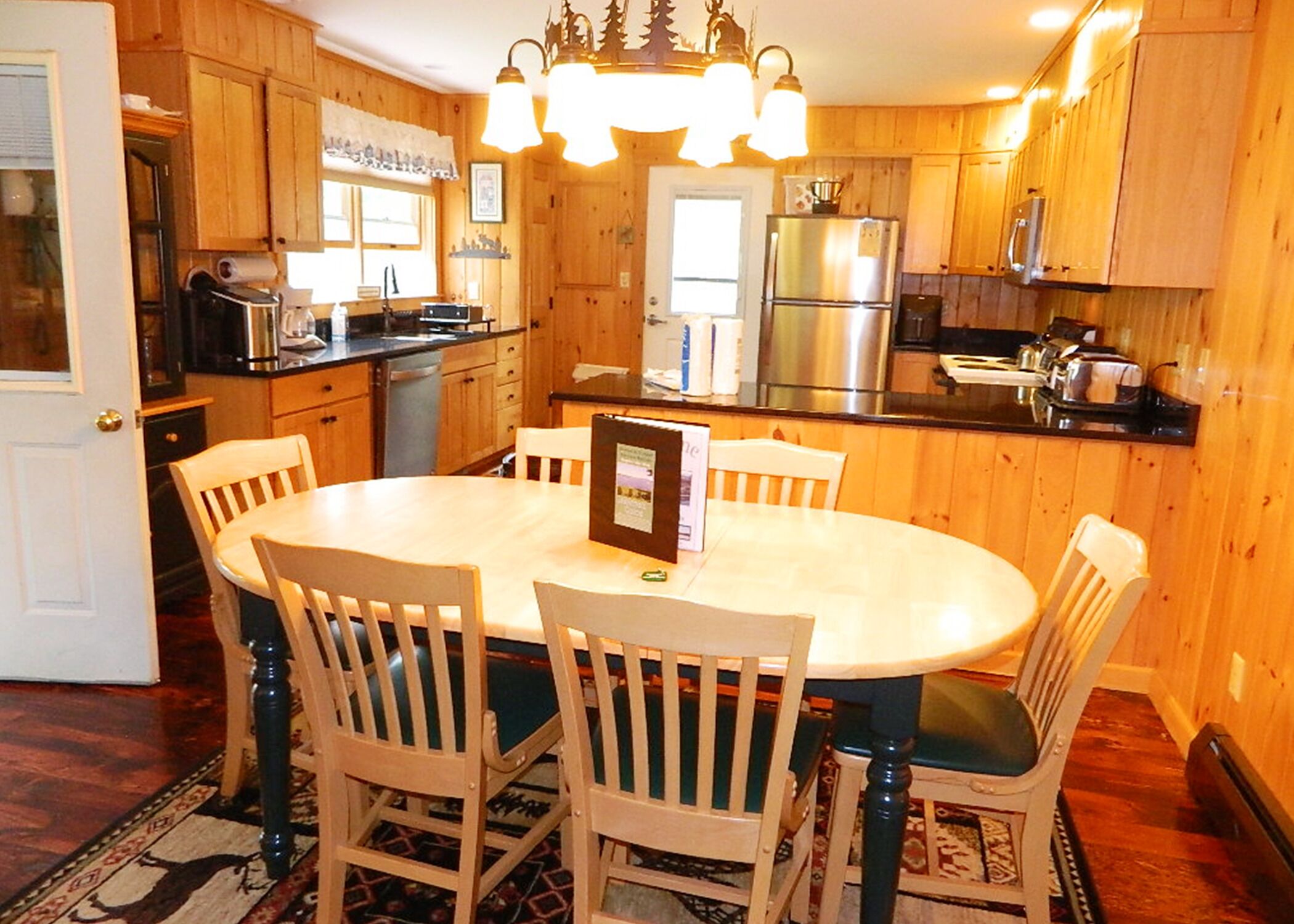 A wooden-paneled kitchen with a round dining table and chairs, a refrigerator, and a stove.