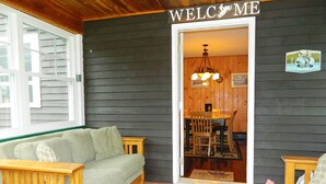 A cozy porch with a wooden bench, a cushioned sofa, and a dining area with a table and chairs. - Rangeley Manor P | 4 Bedroom Cabin with Shared Waterfront Access (Rangeley)