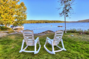 Two rocking chairs facing a lake with a dock and a boat.