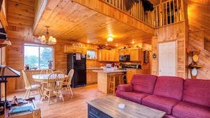 A wooden cabin interior with a dining area, kitchen, and a red sofa. - Mahara 2 - Spacious home with access to Rangeley Lake and the snowmobile trails. (Rangeley)