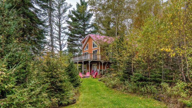 A cabin with a porch and deck, surrounded by dense forest. - Mahara 2 - Spacious home with access to Rangeley Lake and the snowmobile trails. (Rangeley)