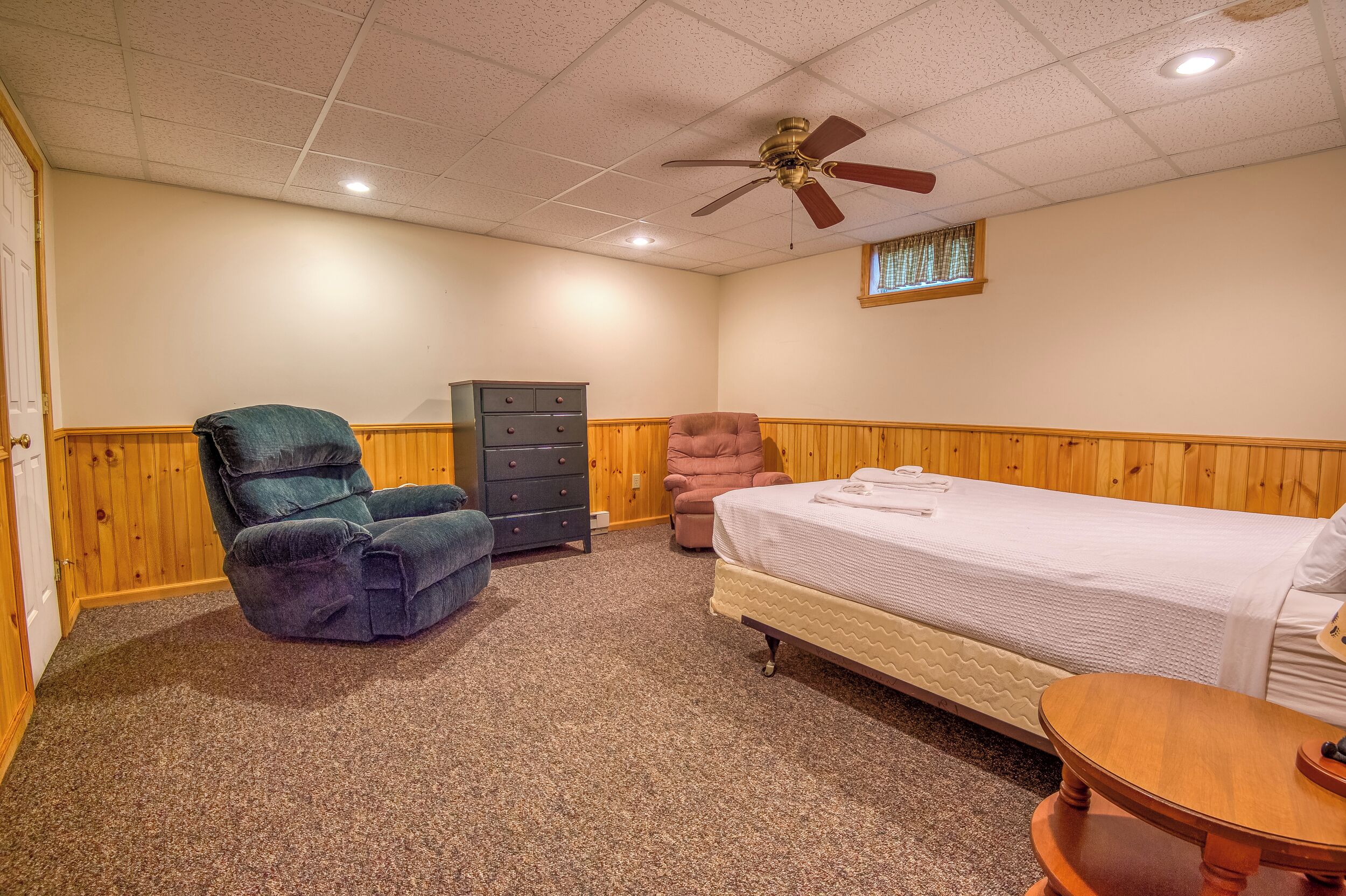 A bedroom with a bed, two chairs, a dresser, and a ceiling fan.