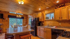 A wooden cabin kitchen with a central island, a refrigerator, a dishwasher, and a stove. - Mahara 2 - Spacious home with access to Rangeley Lake and the snowmobile trails. (Rangeley)