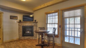 A cozy living room with a stone fireplace, a round wooden table, and two bar stools. - Oquossoc Suite #4 | A/C & Fireplace (Oquossoc)