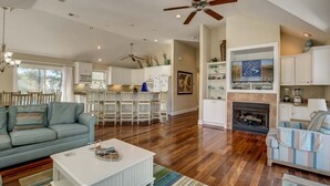 A spacious living area with a large sofa, a coffee table, and a fireplace. There is a kitchen in the background with white cabinets and a bar area. - Jones Beach House | 1200 ft from the beach | Private Pool, Hot Tub | Corolla (Corolla)