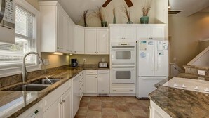 A kitchen with white cabinets, a granite countertop, a built-in oven, a refrigerator, and a window with blinds. - Jones Beach House | 1200 ft from the beach | Private Pool, Hot Tub | Corolla (Corolla)