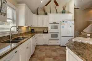 Eine Küche mit weißen Schränken, einer Granit Arbeitsplatte, einem eingebauten Backofen, einem Kühlschrank und einem Fenster mit Jalousien.