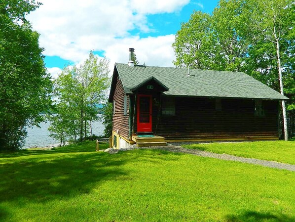 A log cabin with a red door, a chimney, and a grassy yard by a lake. - Rissbern II - Very charming and private setting on over 400ft of frontage on Rangeley Lake (Rangeley)