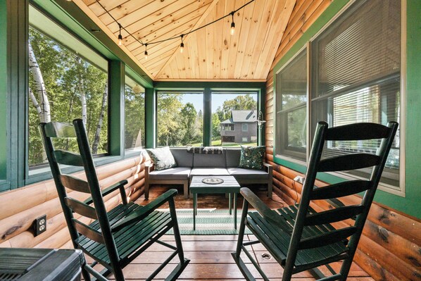A log cabin with a wooden ceiling, a sofa, two chairs, and a table.