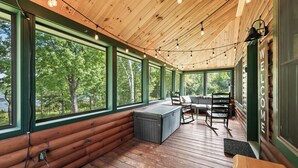 Ein Holzblockhaus-Innenraum mit einer Bank, einem Tisch und einem großen Fenster mit Blick auf Bäume.