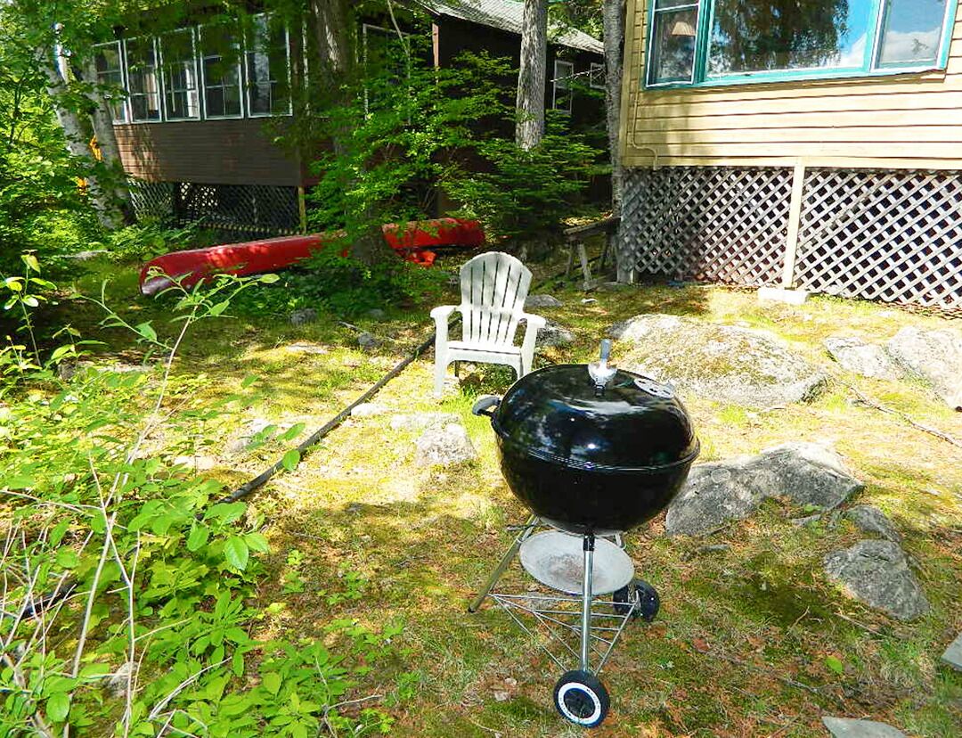 A backyard with a barbecue grill, a white chair, and a red canoe.