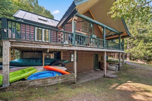 A two-story log cabin with a balcony, outdoor seating, and kayaks stored under the house. - Loon Lake Retreat - Located on Loon Lake, with additional guest cottage for rent as well (Rangeley)