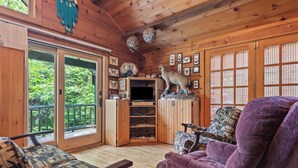 L’intérieur d’un chalet en bois, avec un canapé, un fauteuil à motifs, un téléviseur et une bibliothèque.
