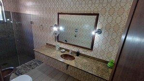 Ein Badezimmer mit einer Wand aus gemusterten Fliesen, einer Arbeitsplatte aus Granit, einem Waschbecken, einem Spiegel und einer Duschkabine.