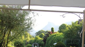 Un espace de restauration en plein air avec une table dressée pour le petit-déjeuner, entourée de chaises, et donnant sur un jardin luxuriant avec une montagne en arrière-plan.