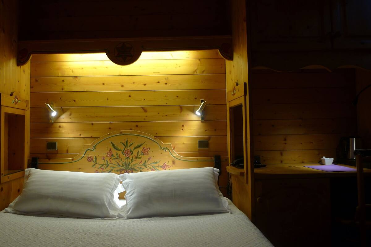 A wooden cabin-style room with a bed, two wall-mounted lights, and a decorative headboard.