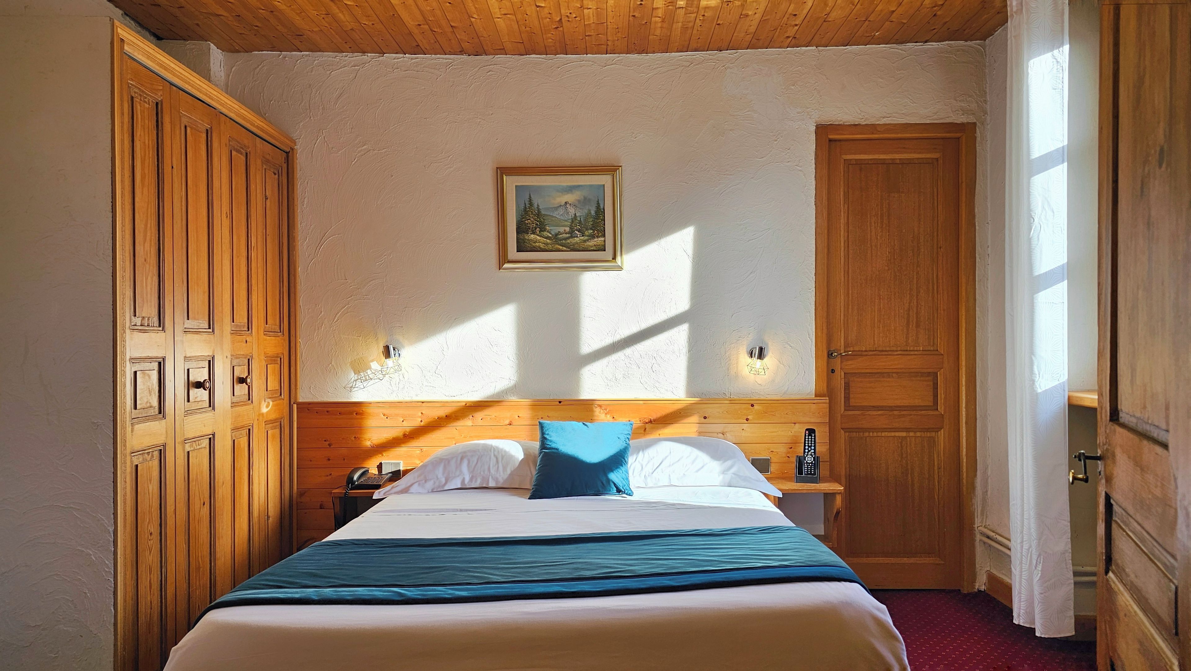 Una habitación de hotel con una cama, un armario de madera, un cuadro en la pared y una puerta.