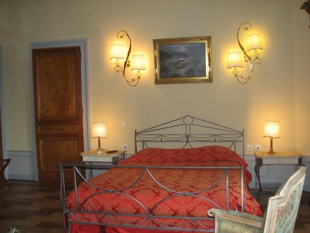 Un dormitori amb un llit de metall, dues taules de nit amb làmpades, una porta de fusta i un quadre al mur.