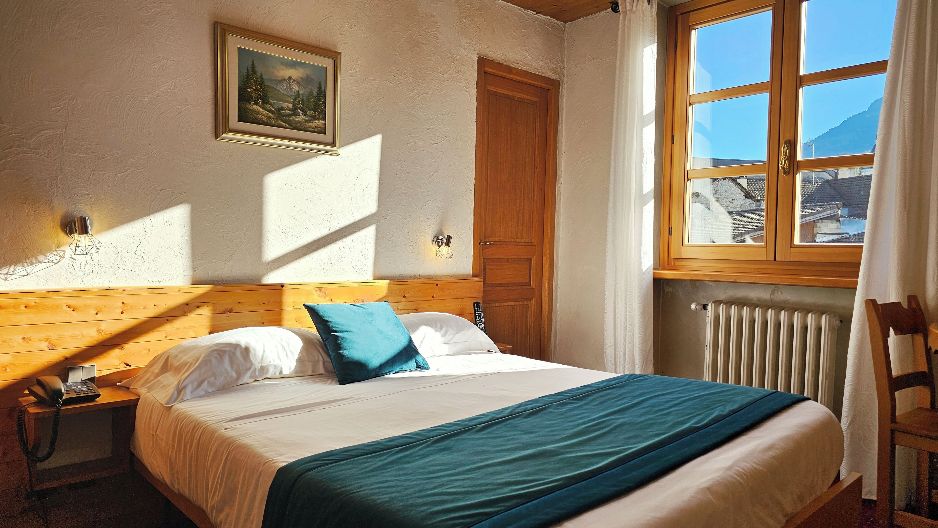 Een slaapkamer met een bed, nachtkastje, telefoon, schilderij aan de muur, raam met uitzicht en een radiator.