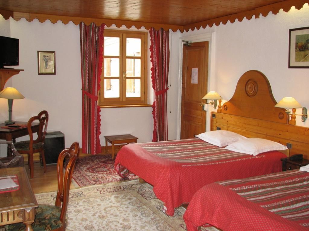 Una habitación con dos camas, cabecero de madera, un escritorio con lámpara, una silla y una ventana con cortinas.