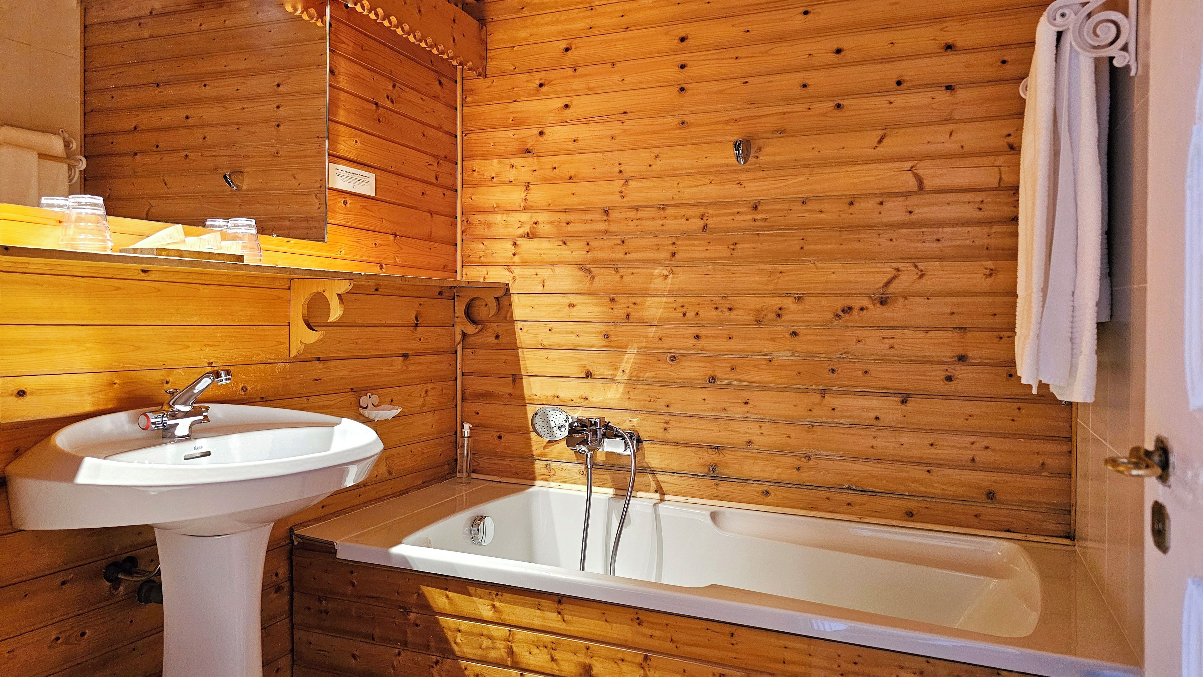 Baño de cabaña de madera con lavamanos, ducha y una toalla colgada en la pared.